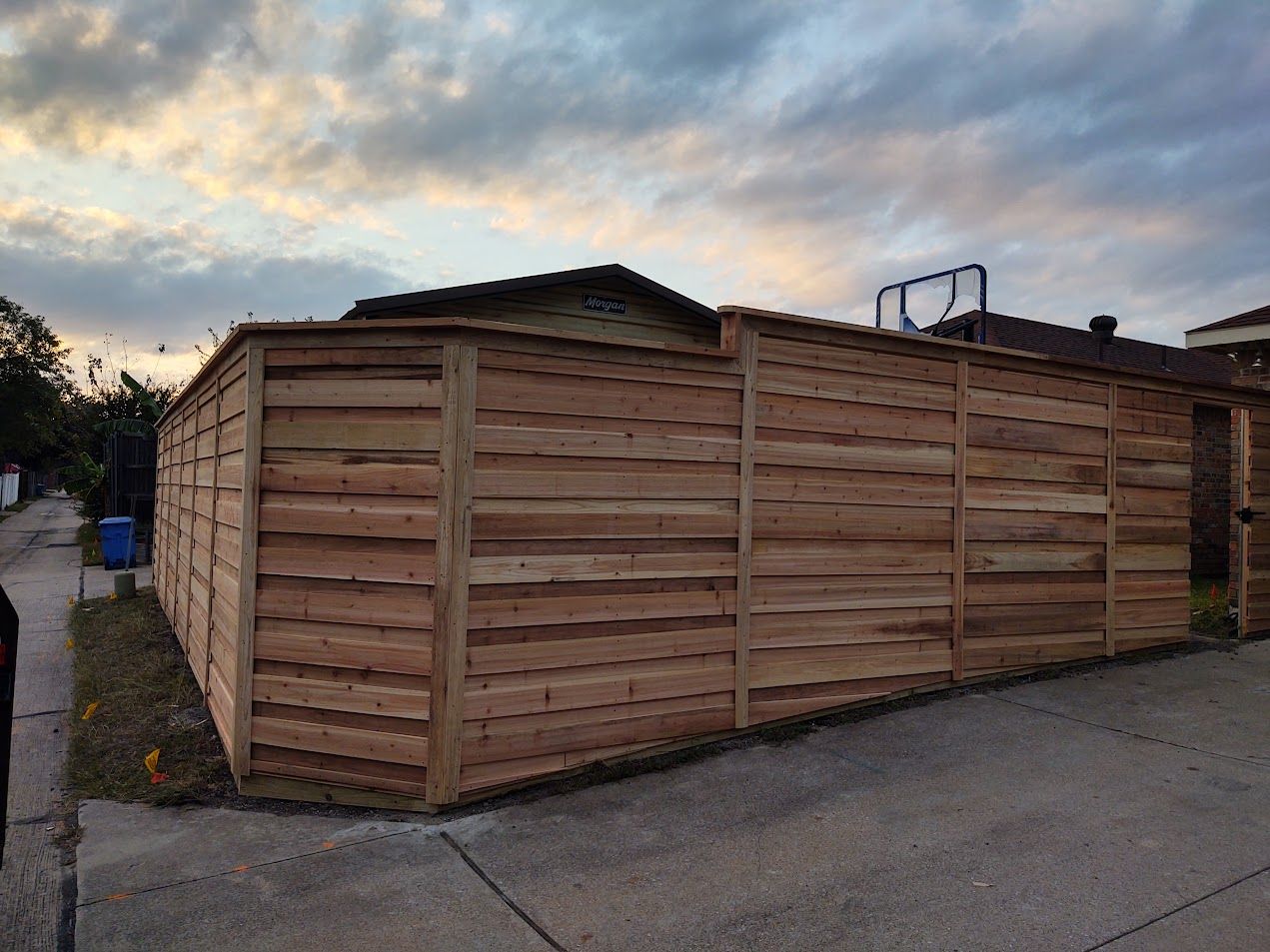 Wooden privacy fence around a corner lot at dusk, with cloudy sky overhead.