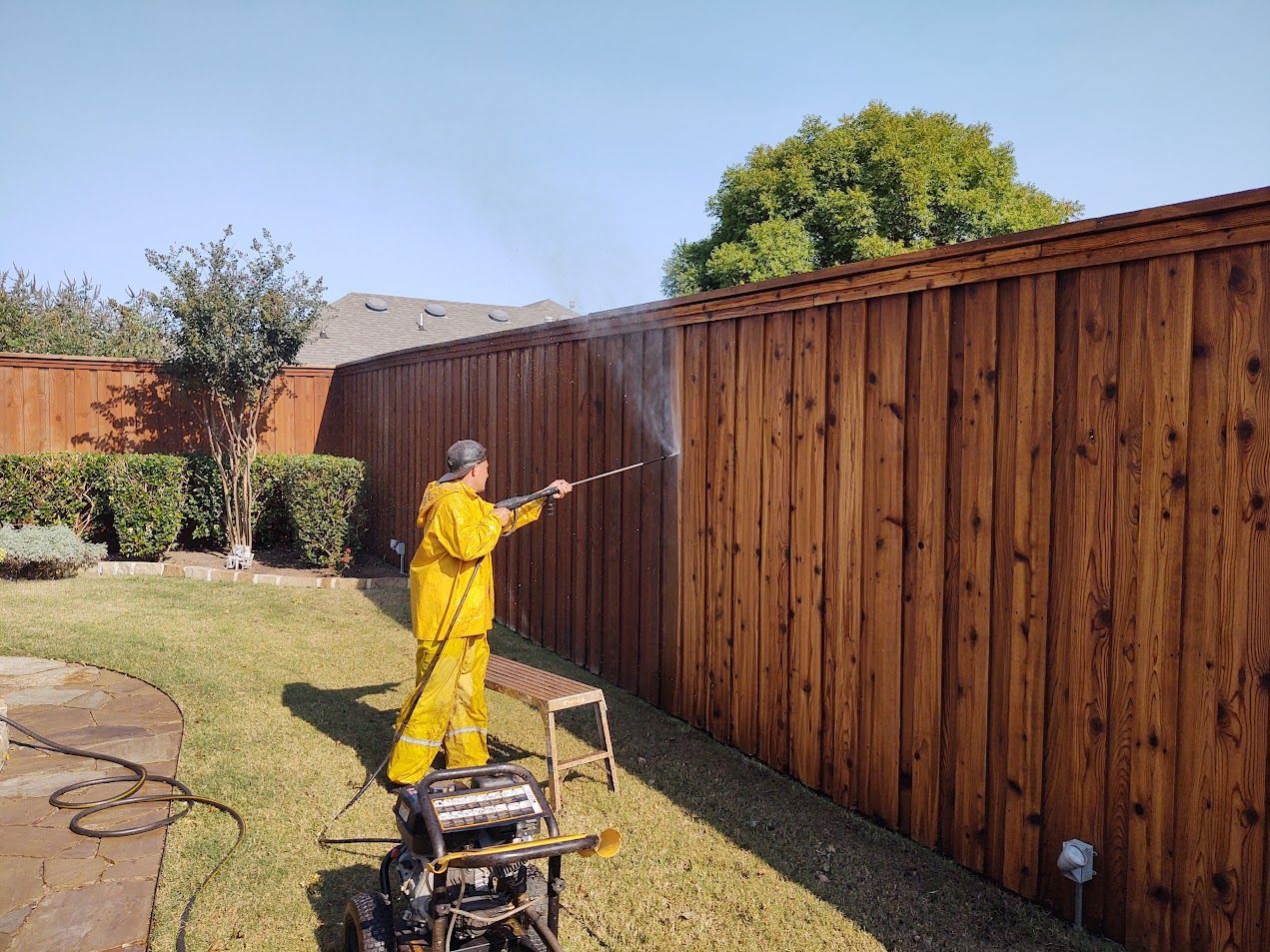Person in yellow spray-painting a wooden fence in a backyard.