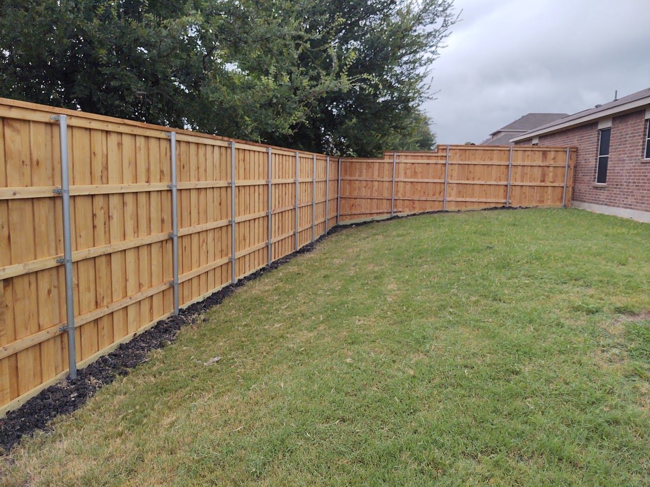Backyard with a wooden privacy fence curving around a grassy lawn beside a brick house
