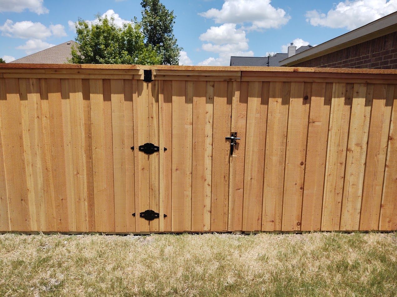 Wooden backyard fence with black hinges and latch under a blue sky with clouds