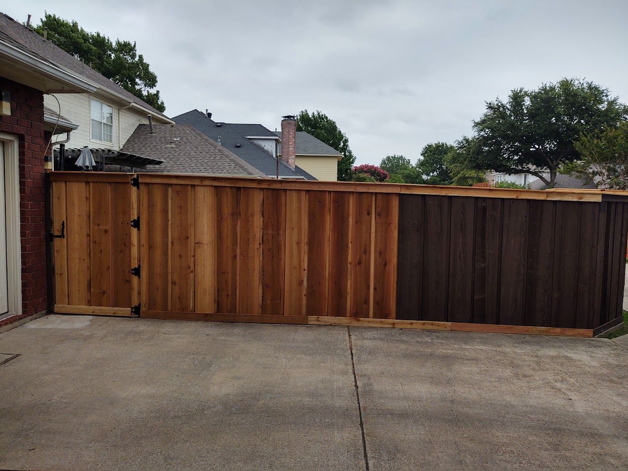 Wooden driveway gate with mixed brown panels beside a concrete driveway and suburban houses