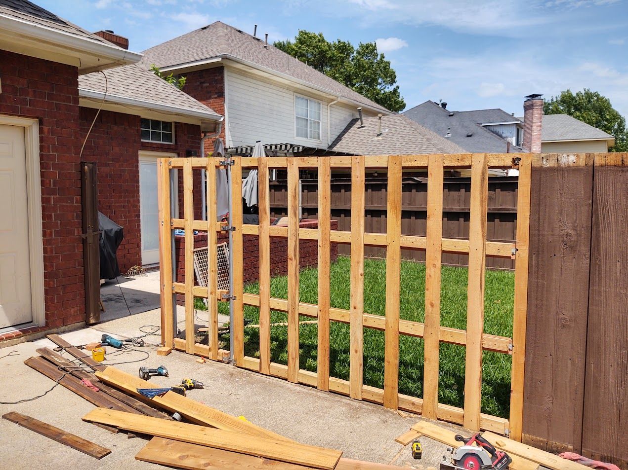 Partially built wooden fence in a backyard, with tools and lumber on the ground