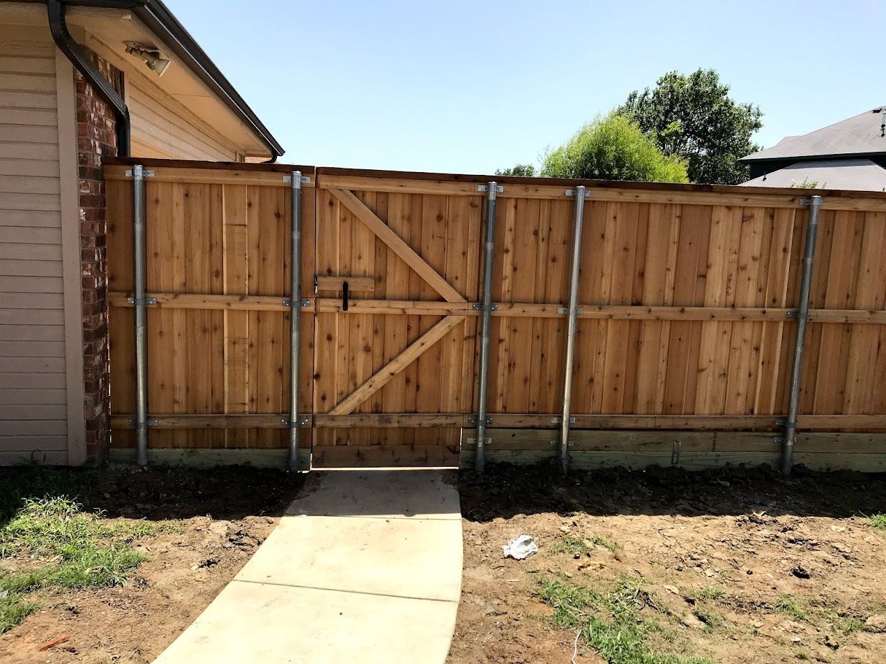 Wooden backyard fence and gate beside a concrete walkway on a sunny day