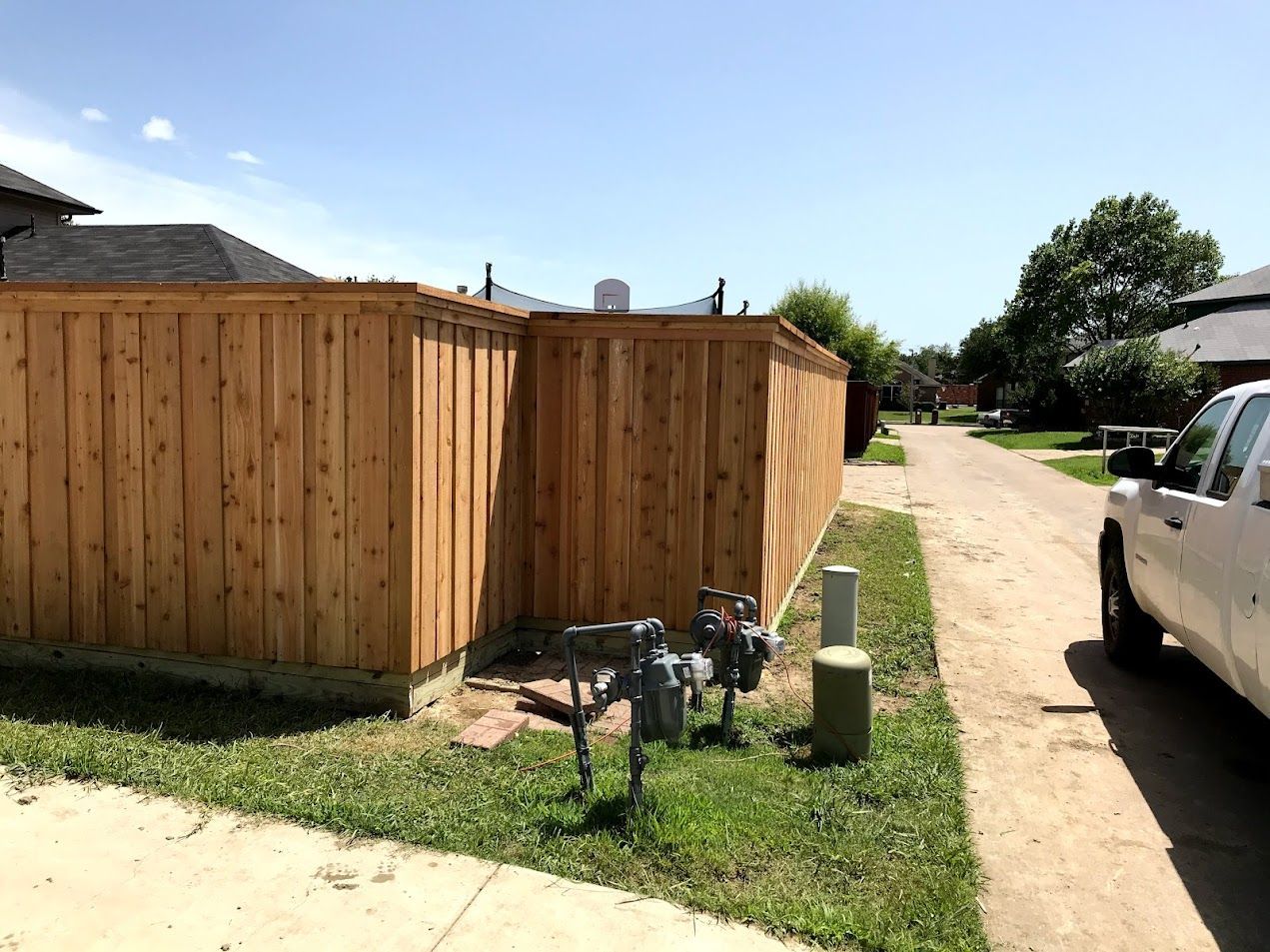 Wooden privacy fence beside a dirt driveway with a white truck parked nearby.