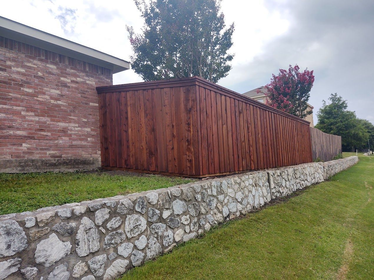 Wooden fence beside a brick wall above a stone retaining wall on a grassy slope