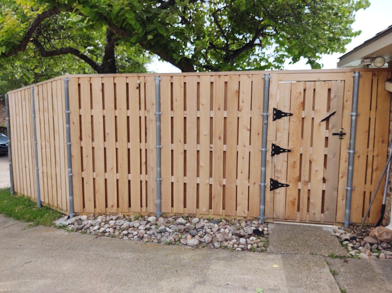 Wooden privacy fence with a gate along a driveway, bordered by gravel and grass.