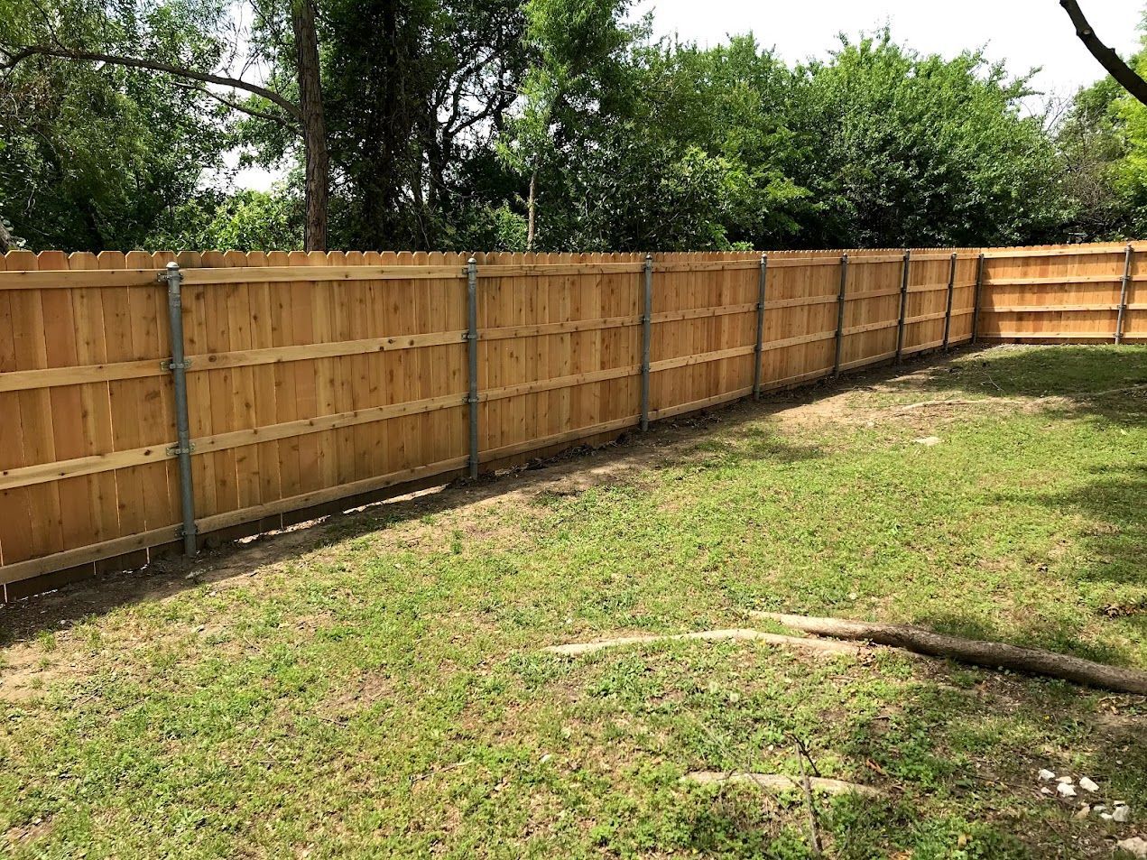 Wooden privacy fence along a grassy yard with trees in the background