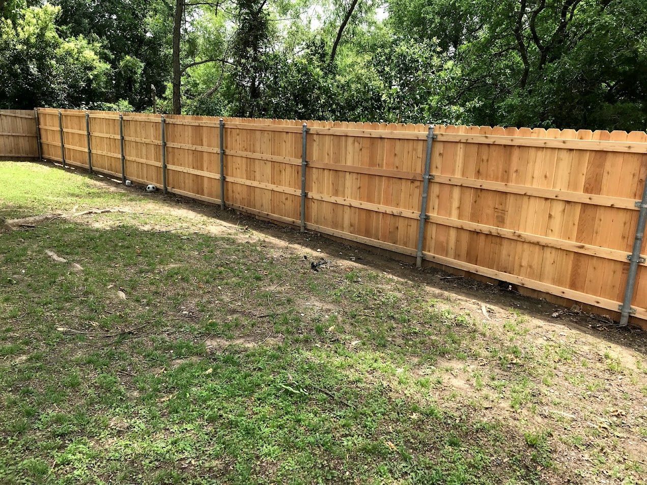 Wooden privacy fence along a grassy backyard with trees in the background