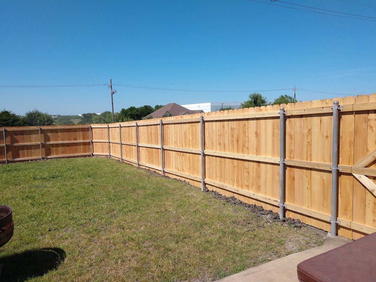 Backyard with a wooden privacy fence, green lawn, and clear blue sky