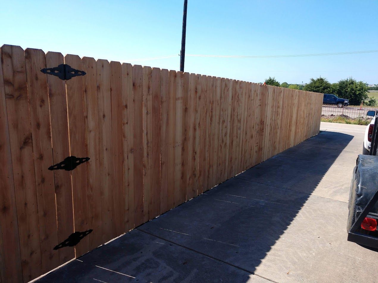 Wooden privacy fence along a sidewalk beside a street on a sunny day