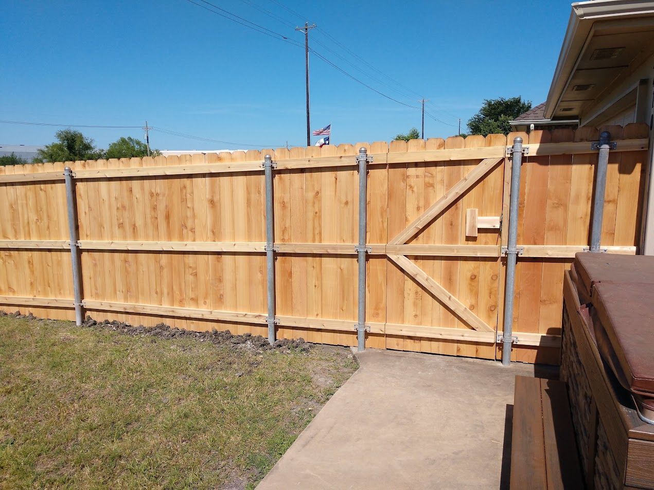 Wooden backyard fence with gate beside a concrete walkway under a clear blue sky