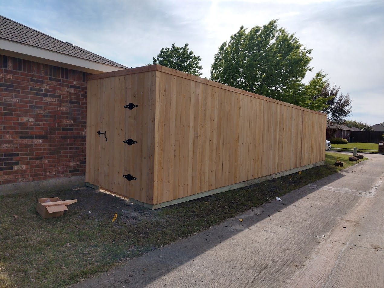 Wooden shed or fence structure beside a brick house along a residential driveway