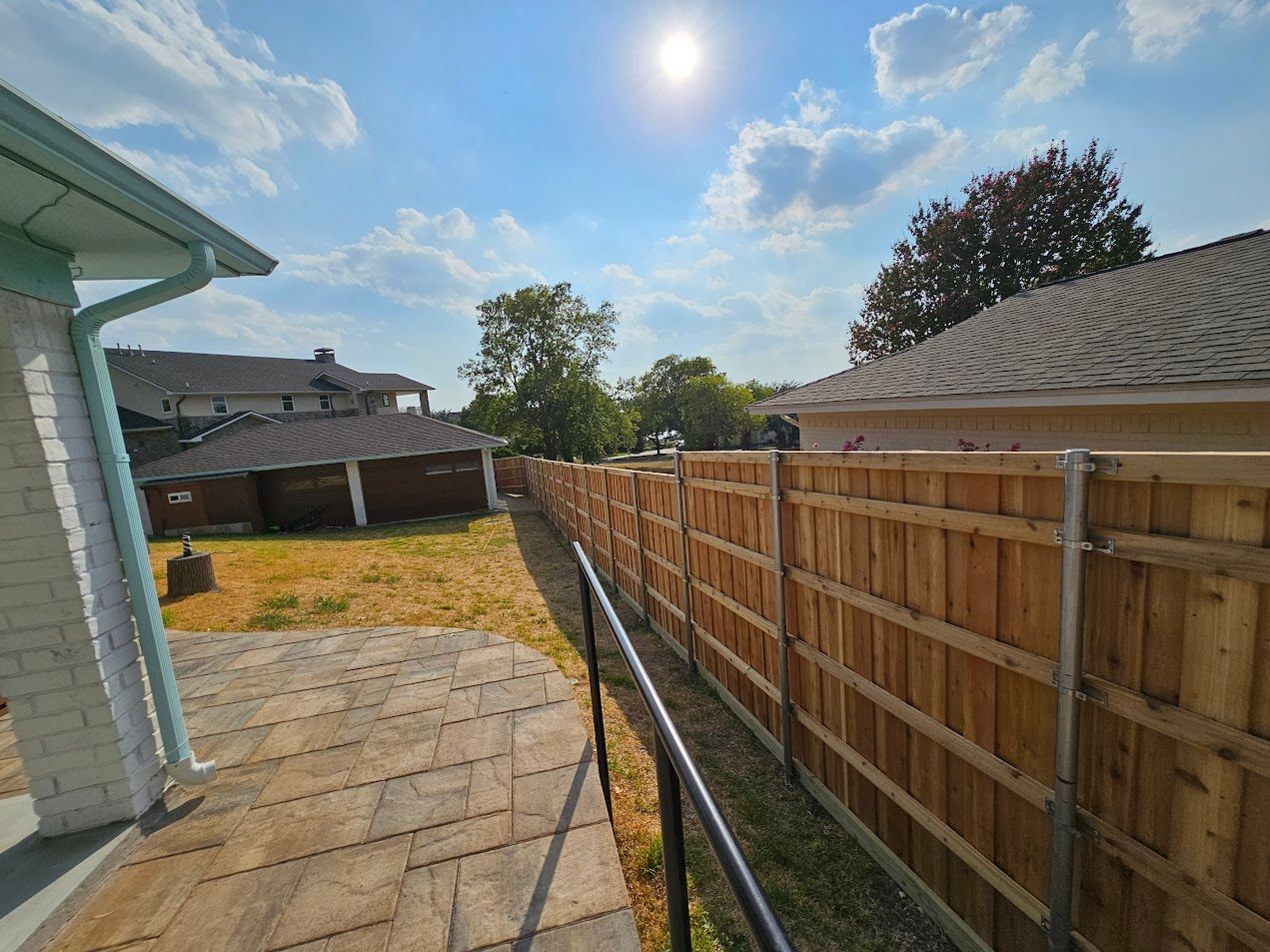 Backyard patio beside a wooden privacy fence under a bright blue sky