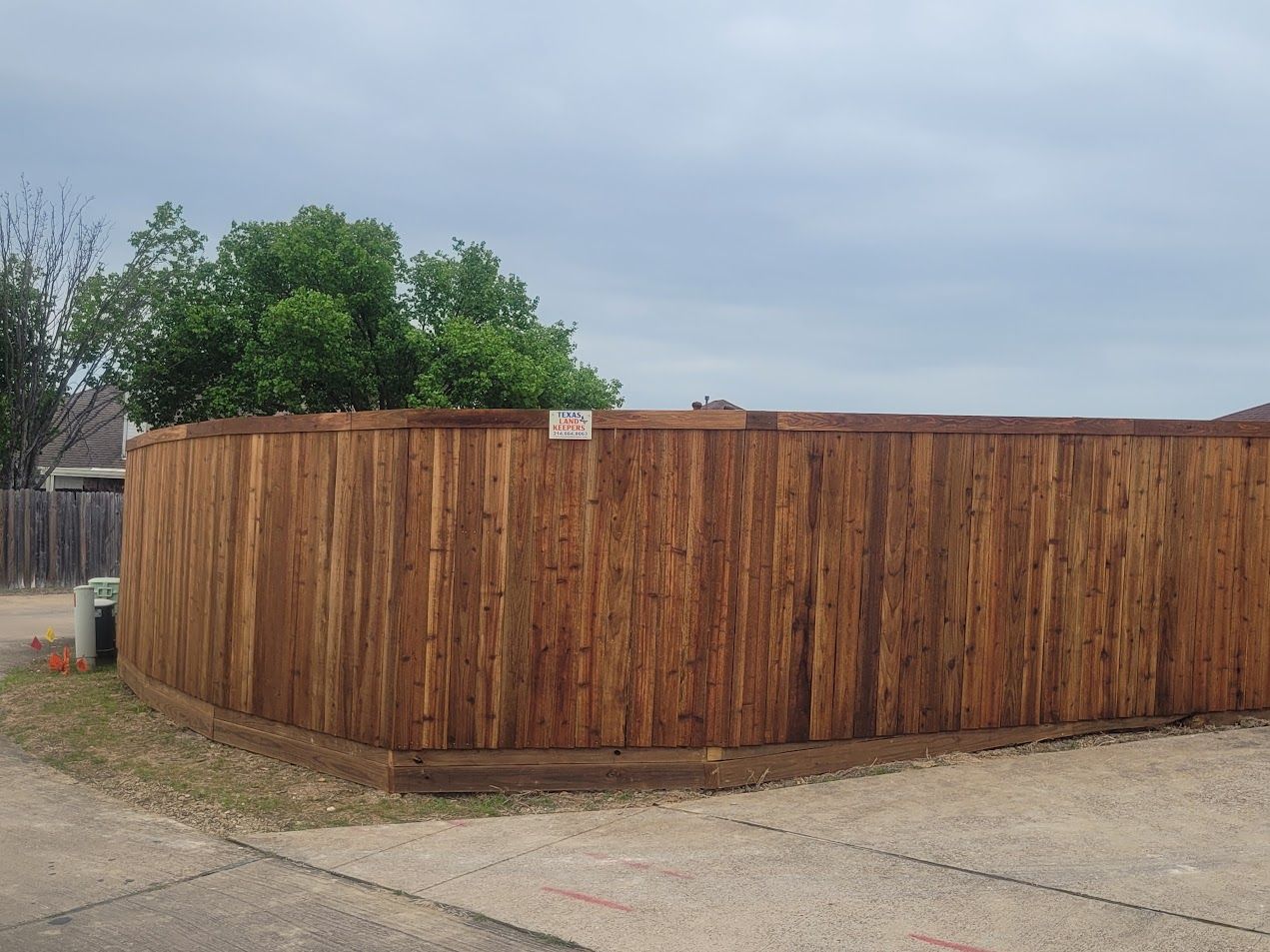 Wooden privacy fence surrounding a corner lot beside a concrete driveway under a cloudy sky