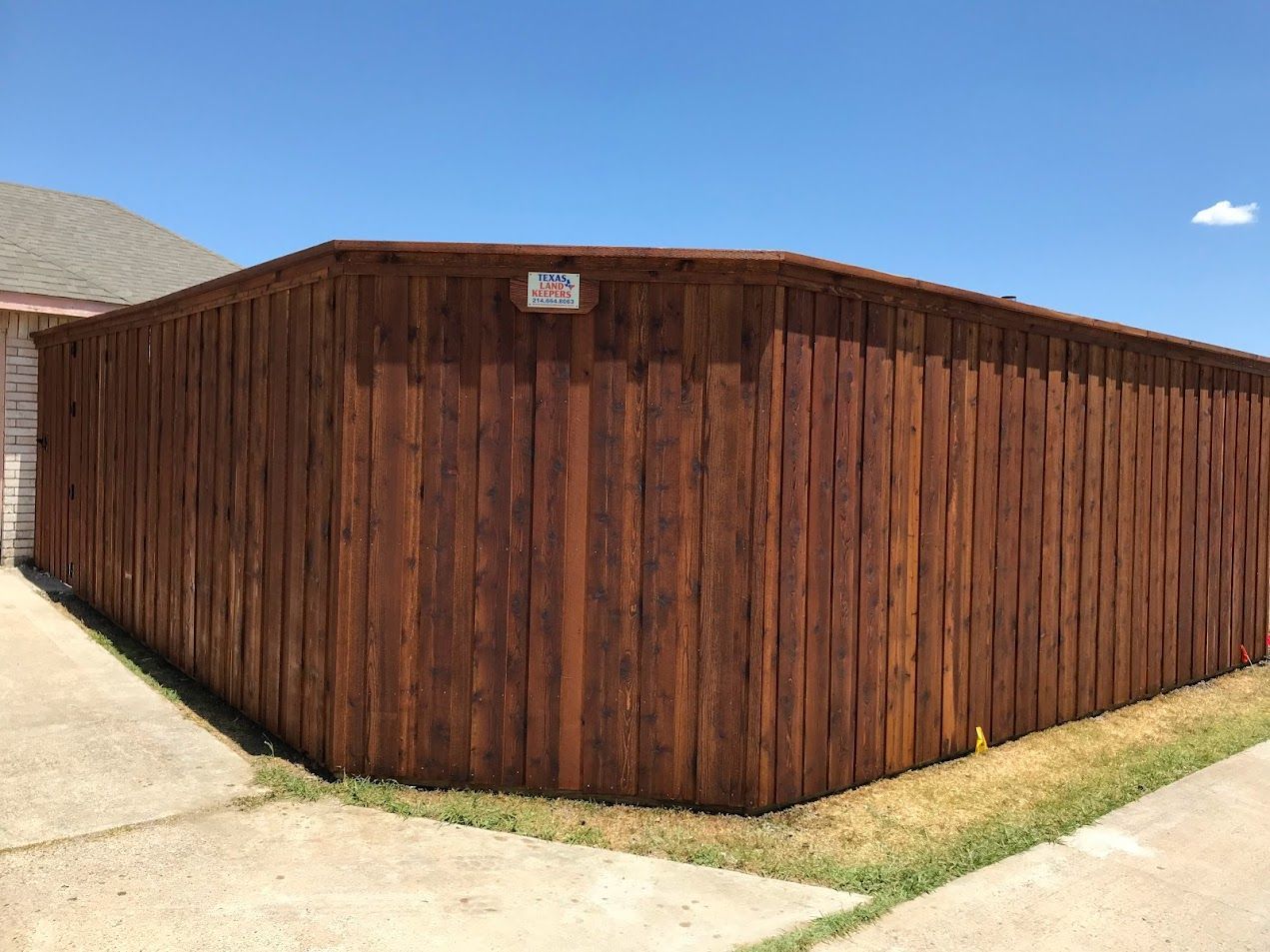 Wooden privacy fence beside a concrete driveway under a clear blue sky