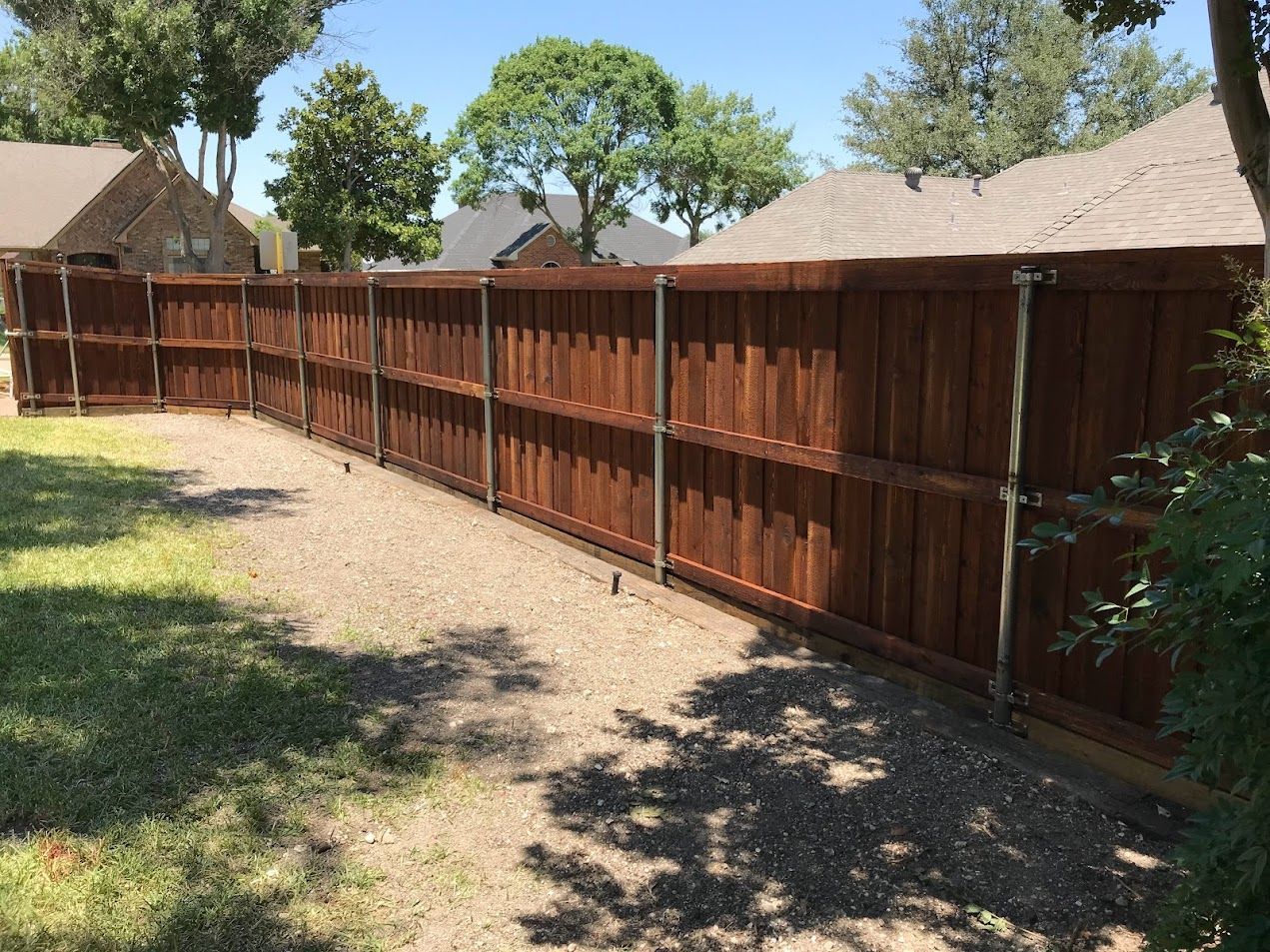 Long wooden fence along a gravel yard with trees and houses in the background