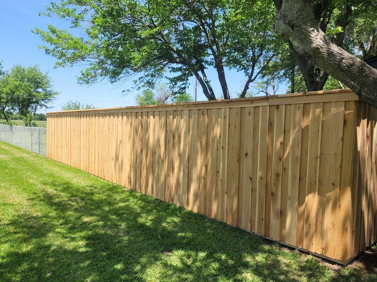 Wooden privacy fence along a grassy slope with trees and blue sky above