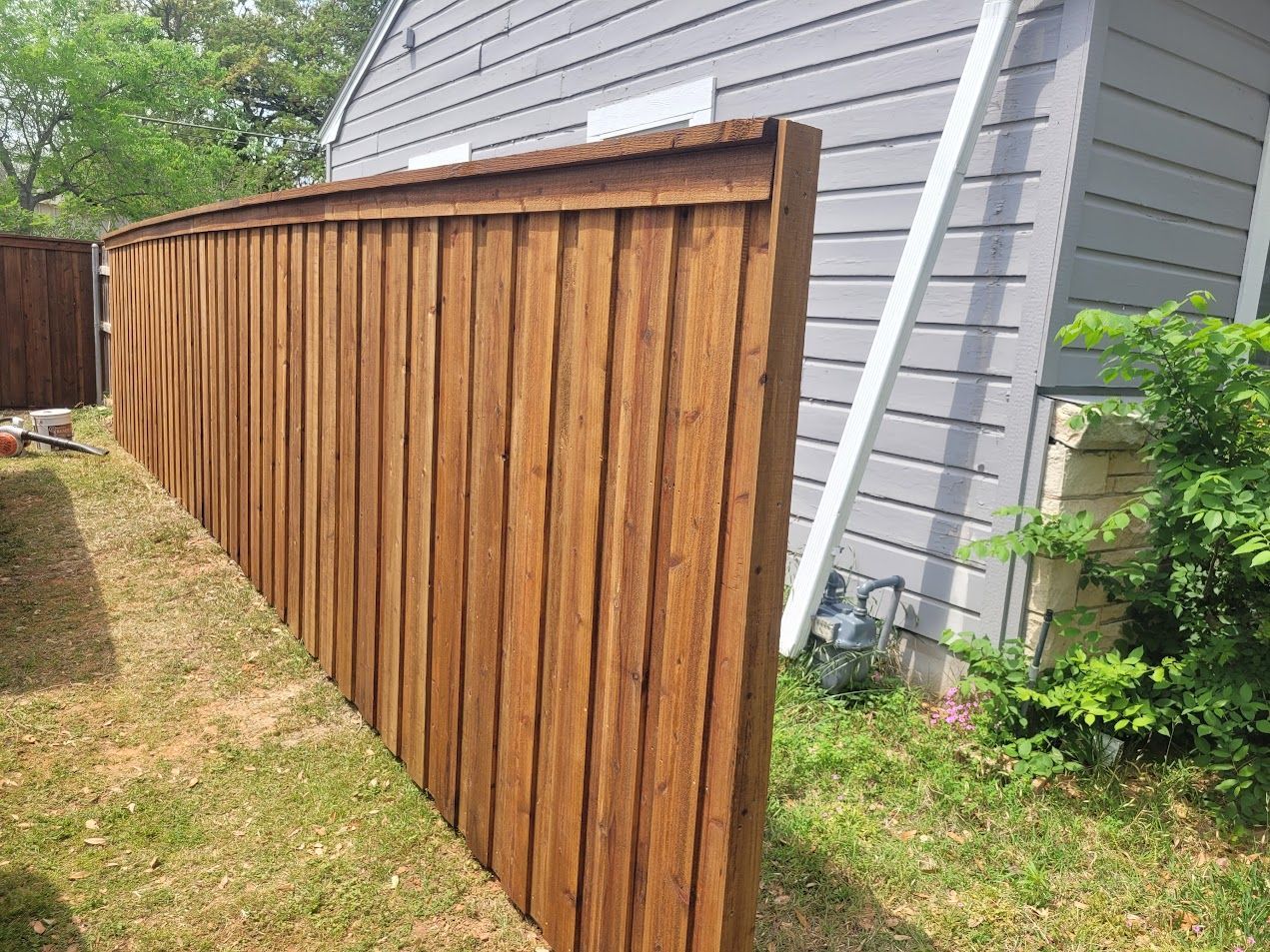 Wooden privacy fence beside a gray house in a grassy backyard.