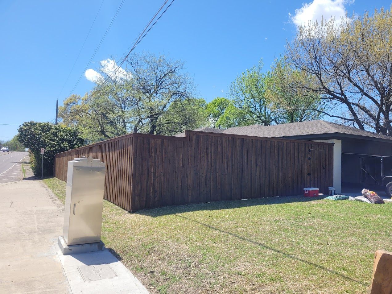 Suburban house with wood fence, grassy yard, sidewalk, and blue sky on a sunny day