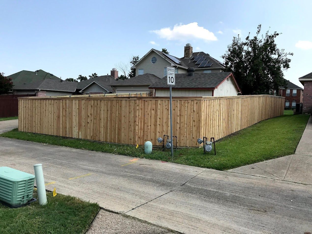 Wooden fence around a corner lot beside a street, with houses and grass in the background.