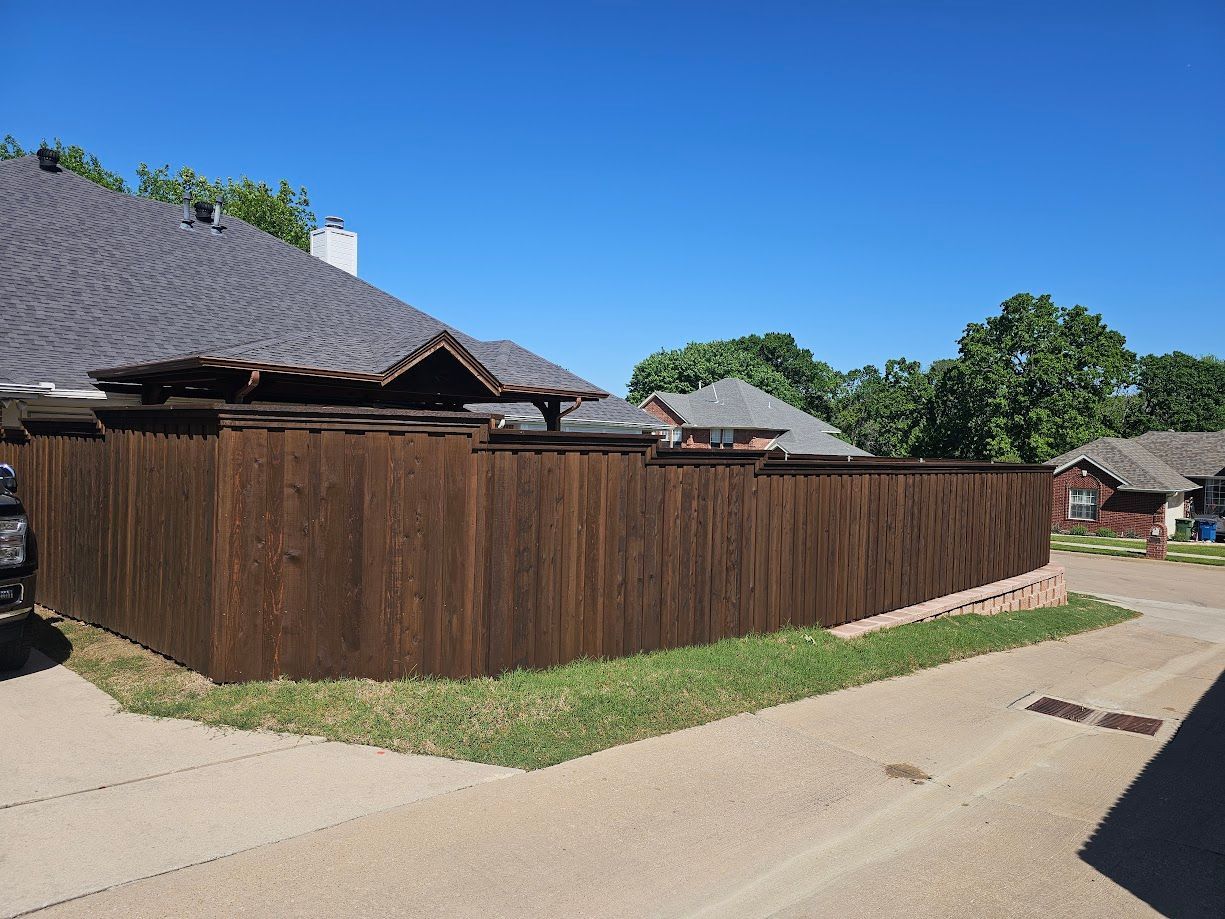 Wooden privacy fence along a driveway beside suburban houses under a clear blue sky