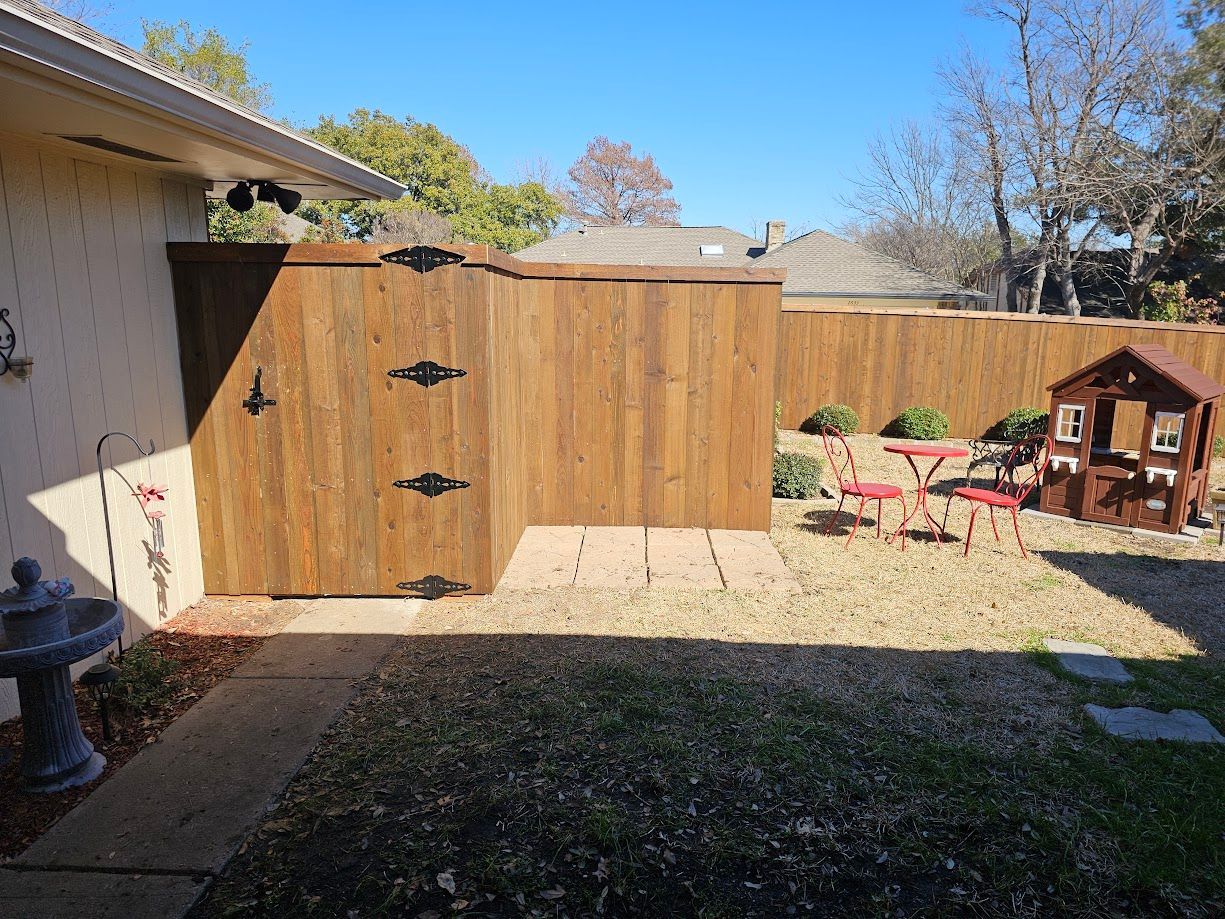 Backyard with wooden gate, gravel patio, red chairs, and small playhouse beside a house