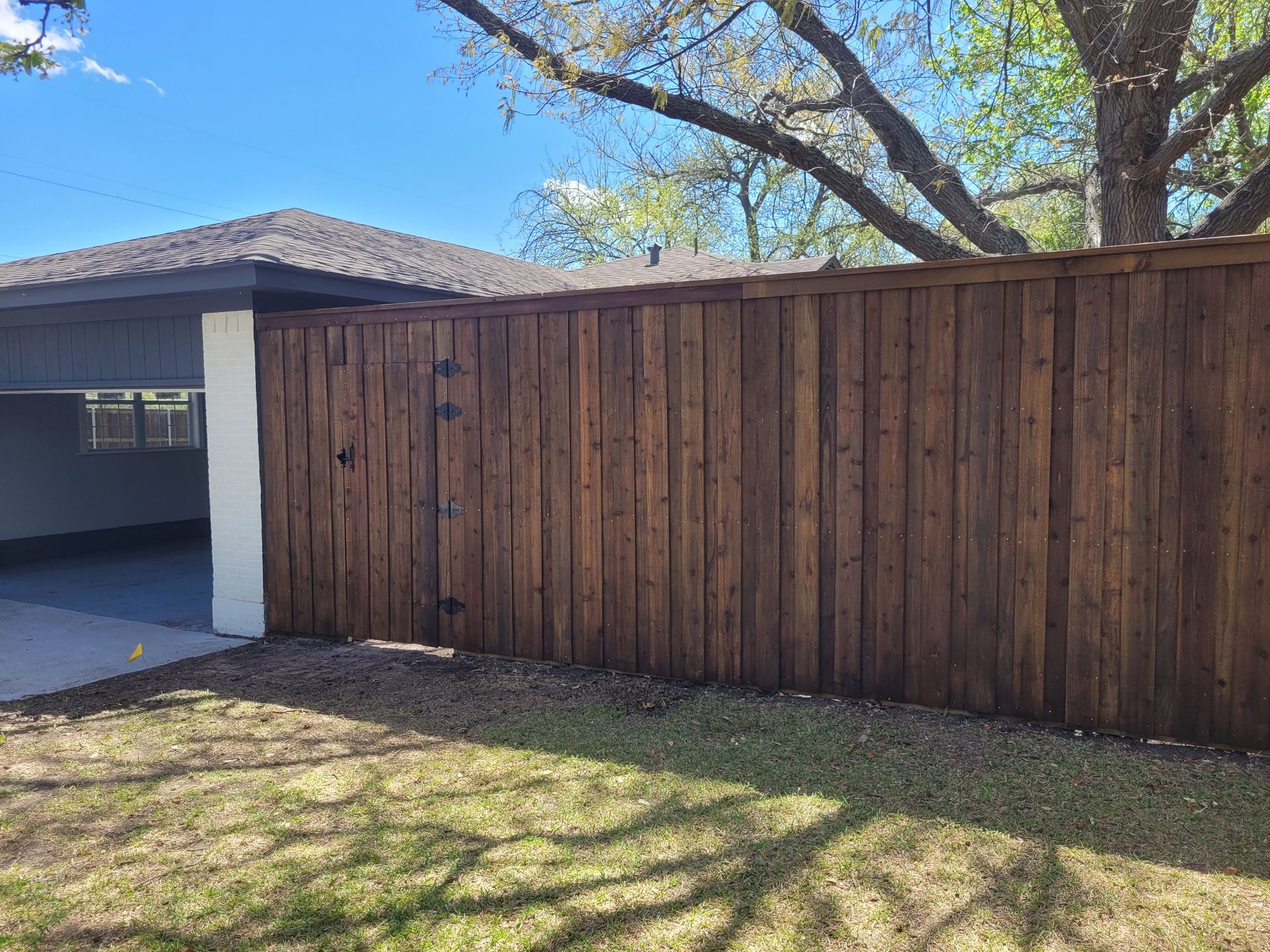 Wooden privacy fence beside a house with a garage, under a blue sky and tree branches.