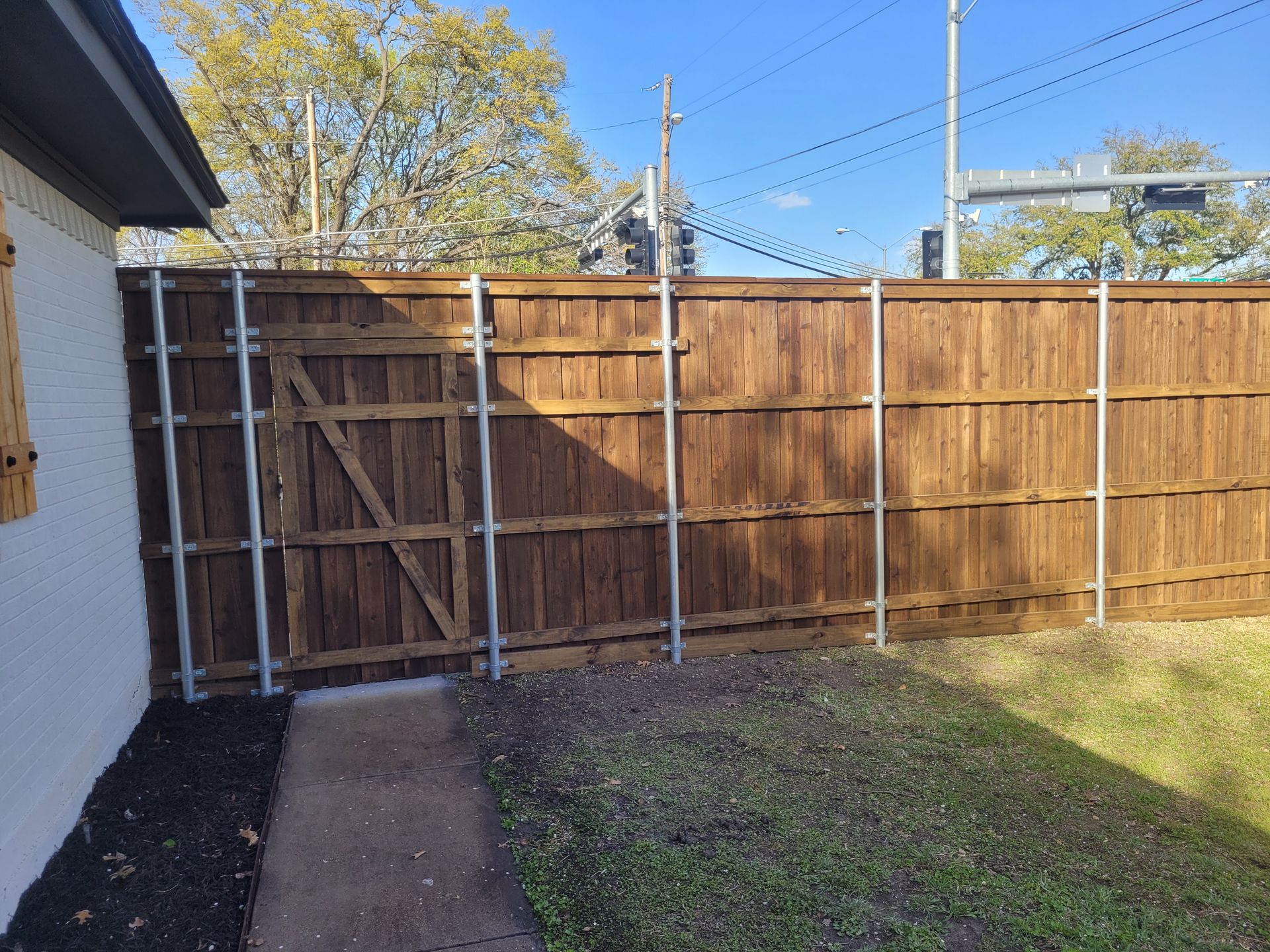 Backyard with a wooden fence and gate beside a house, grass lawn, and concrete walkway.