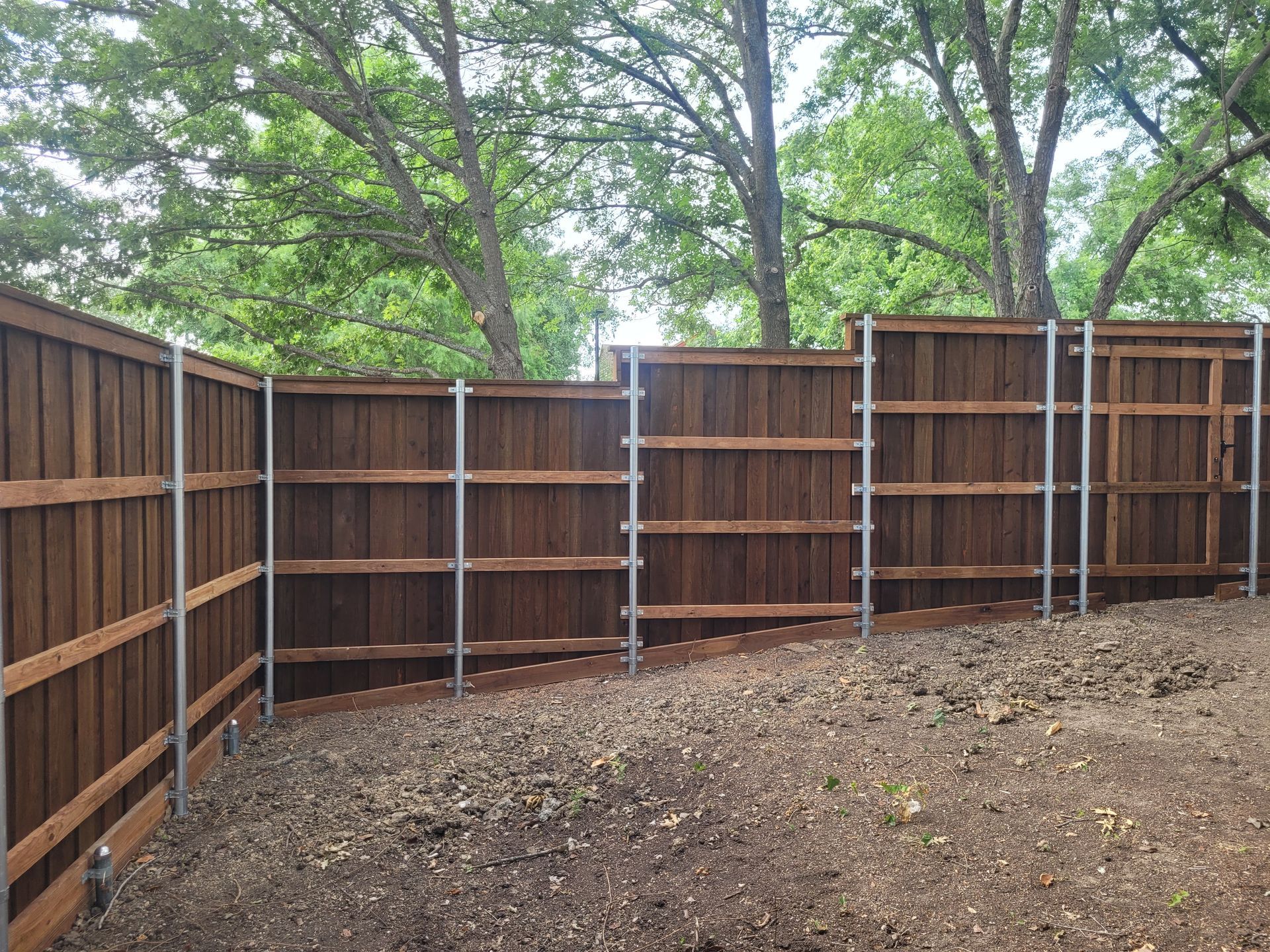 Wooden privacy fence enclosing a bare dirt yard with trees visible beyond it