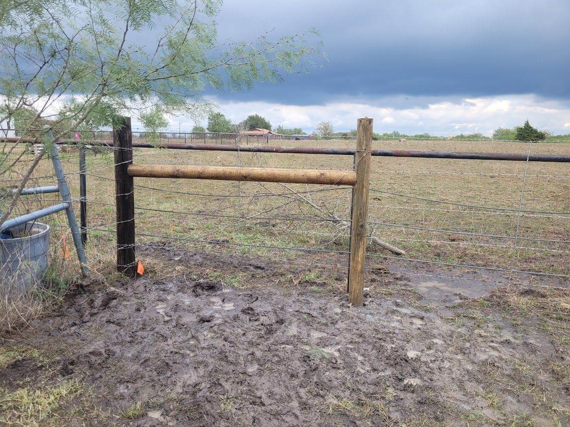 Wooden farm gate and fence beside a muddy field under cloudy skies