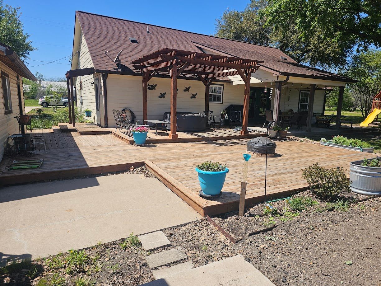 Patio with pergola, potted plants, and a small house in a sunny backyard.
