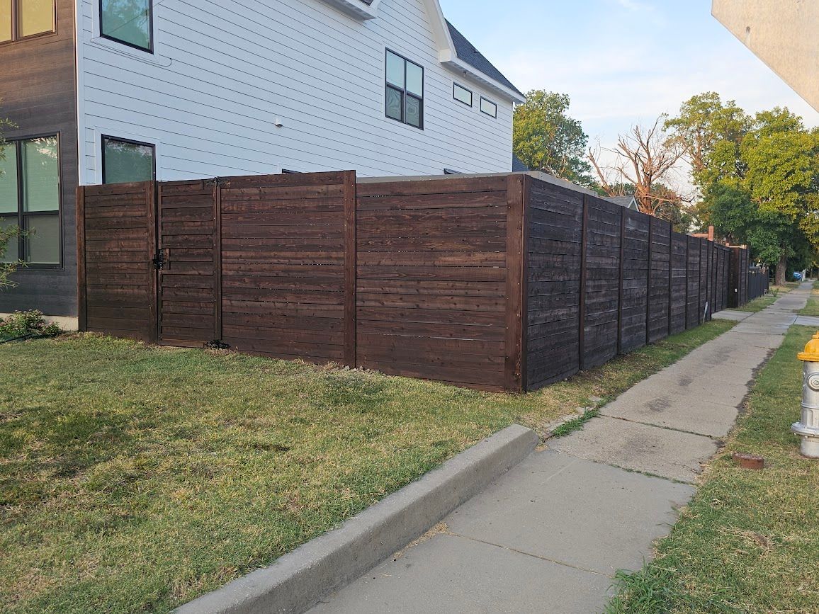 Wooden privacy fence along a sidewalk beside a white house and grassy yard