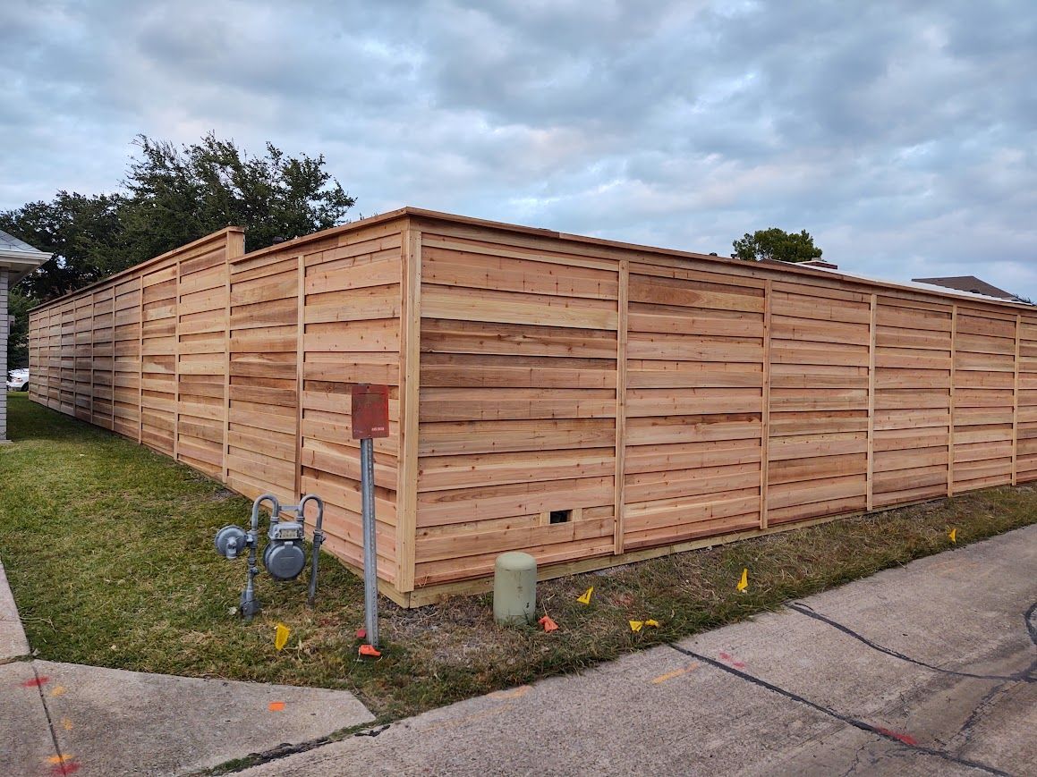 Wooden privacy fence enclosing a corner lot beside a sidewalk and street, under a cloudy sky