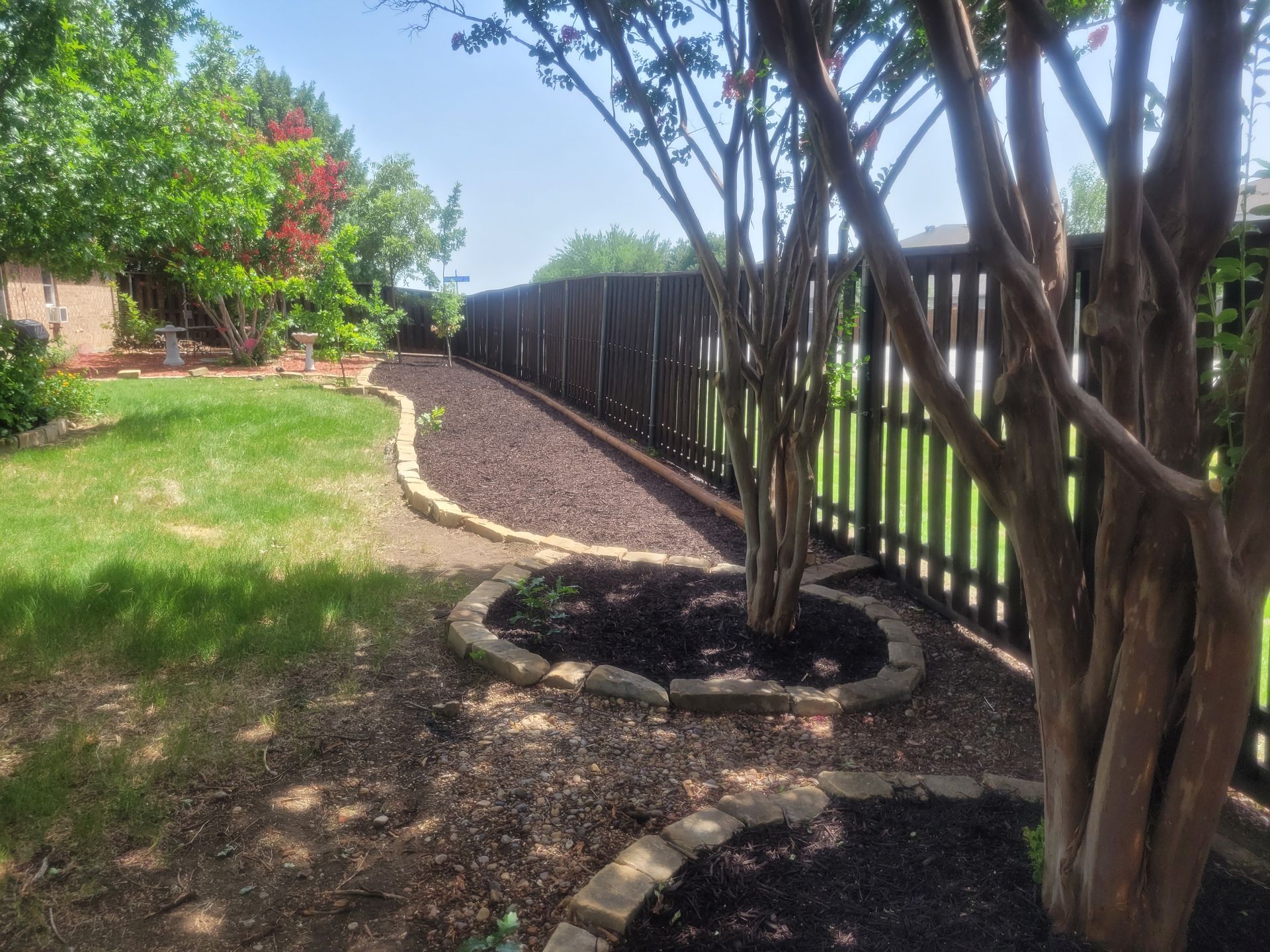 Landscaped backyard path with gravel, trees, grass, and a wooden fence