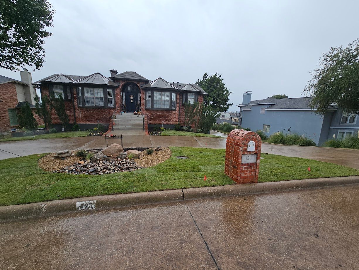 Front yard with a brick house, wet driveway, and a small red mailbox on a rainy day