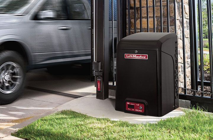 Black gate opener beside a sliding driveway gate as a silver SUV passes through