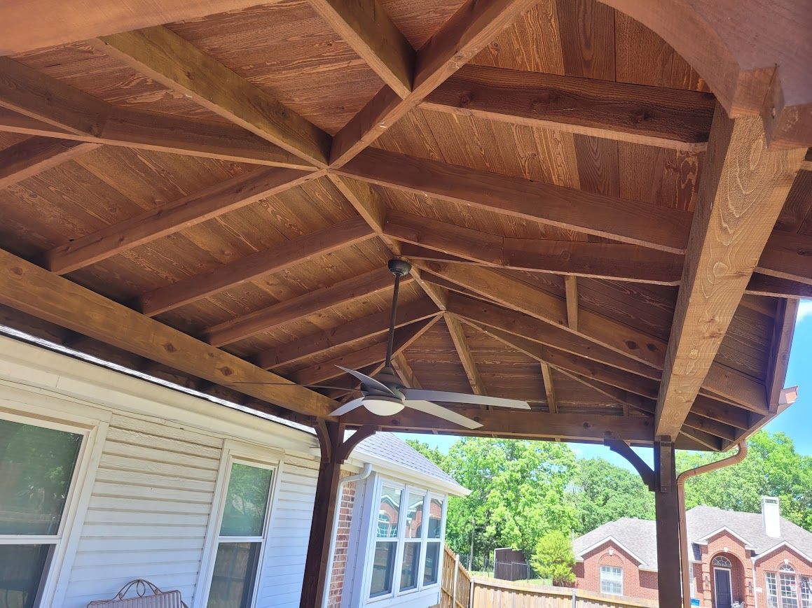 Covered wooden porch roof with exposed beams above a house, with neighboring homes visible in the background