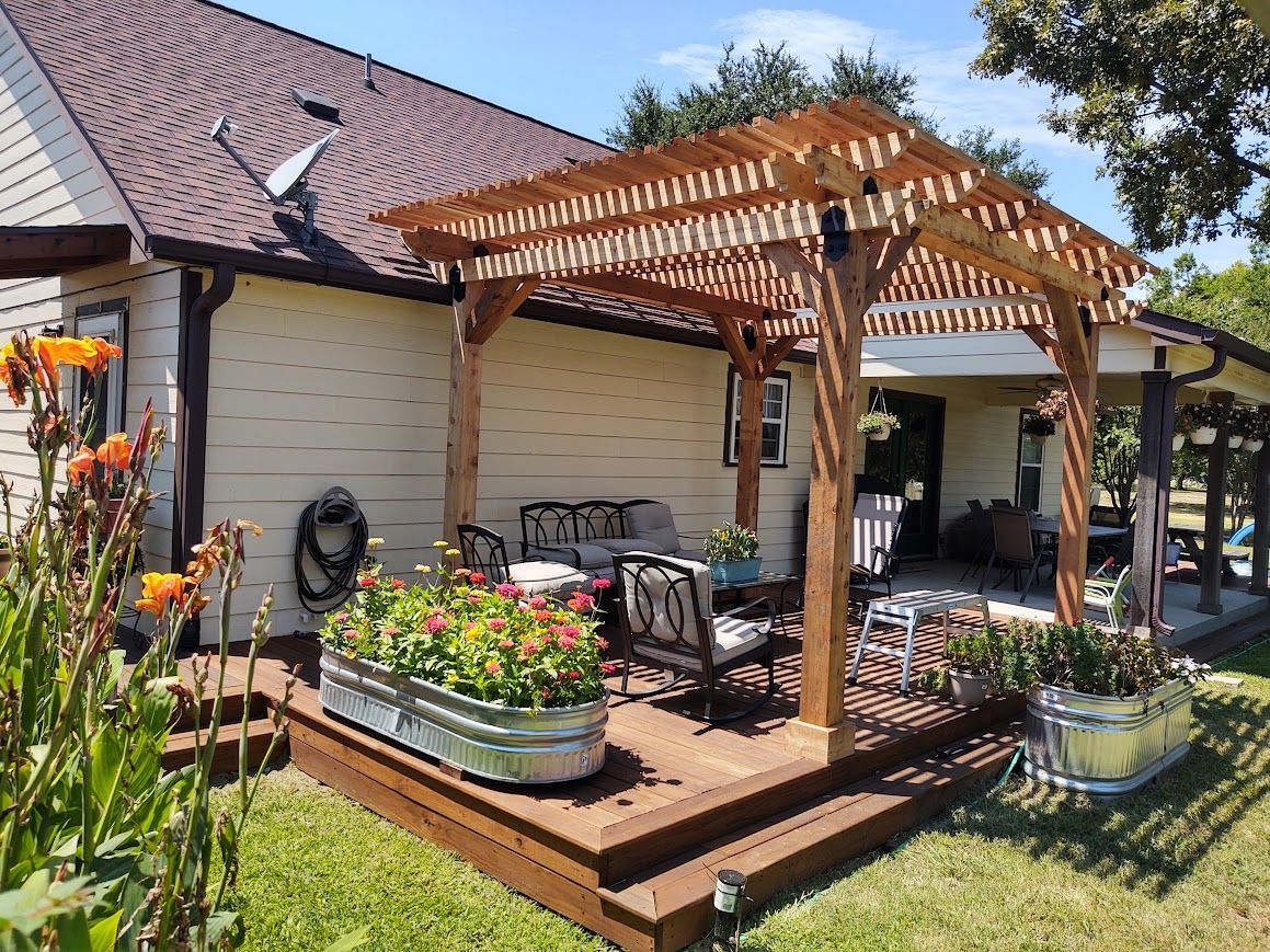 Wooden pergola on a backyard deck with potted flowers beside a house