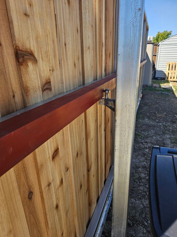 Close-up of a wooden fence with a red horizontal brace beside a white gate post.