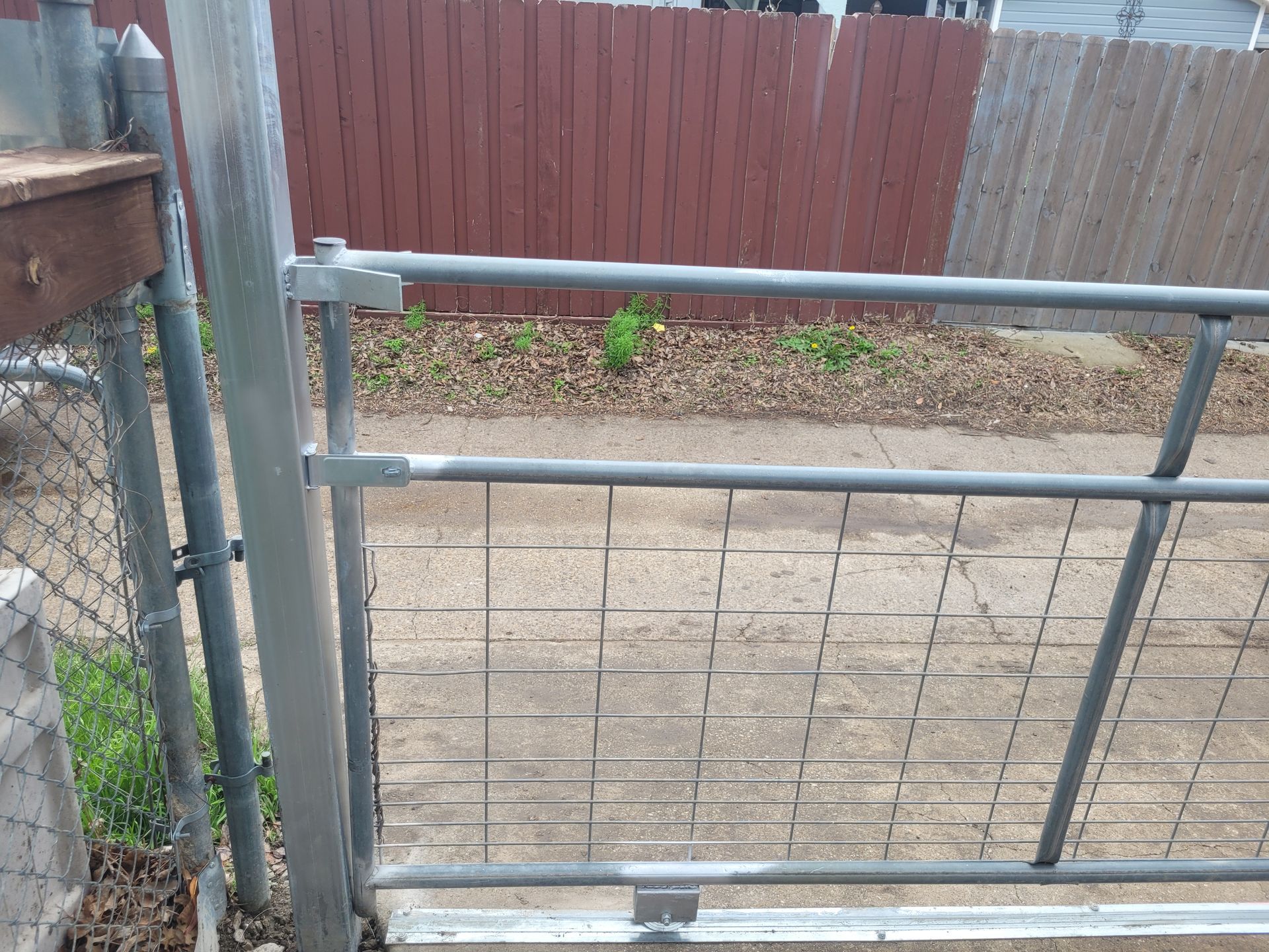 Metal gate and chain-link fence beside a red wooden fence in a backyard.