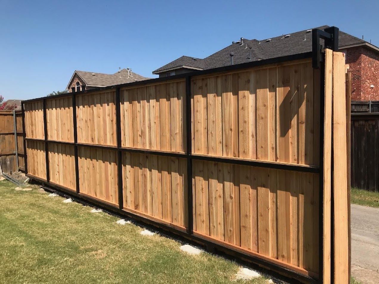 Wooden privacy fence with black posts along a suburban yard under a clear sky