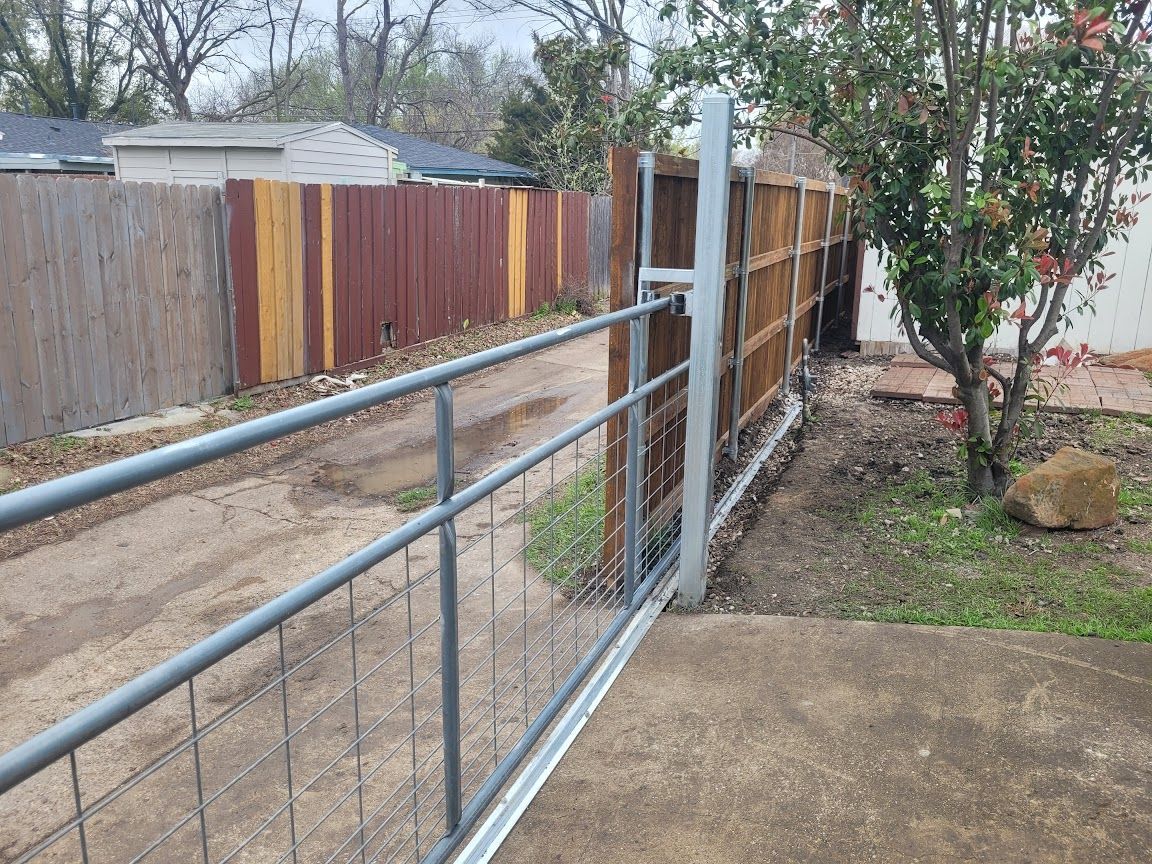Metal ramp and gate beside a wooden fence in a backyard, with a concrete patio and trees.
