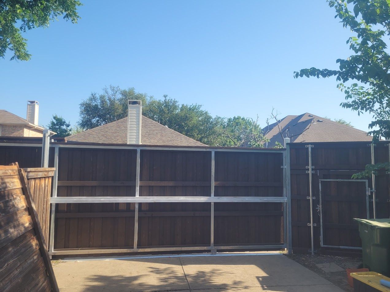 Backyard with a wooden fence, open gate, and clear blue sky above.