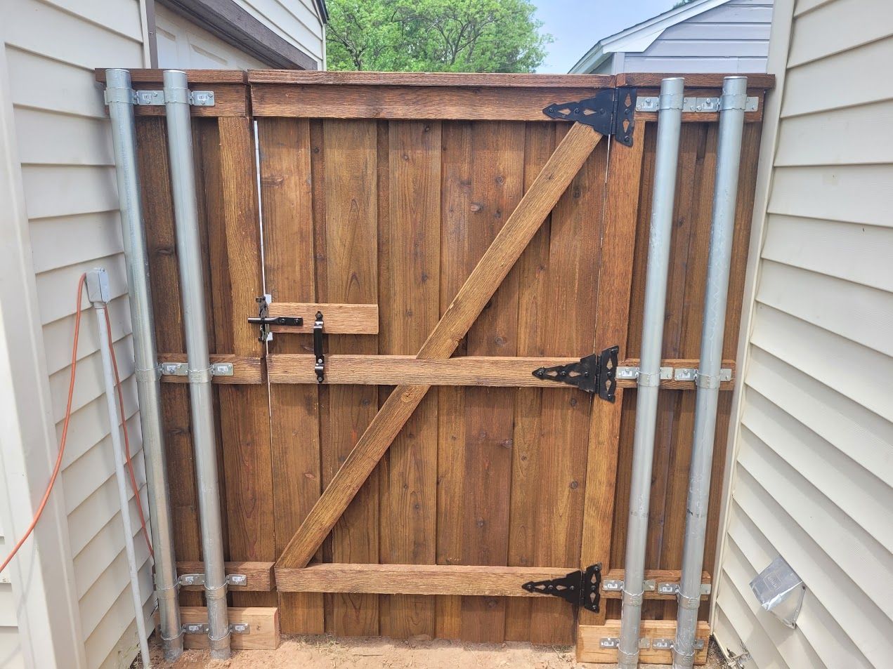 Wooden gate with diagonal braces and metal latches between two houses in a narrow passage