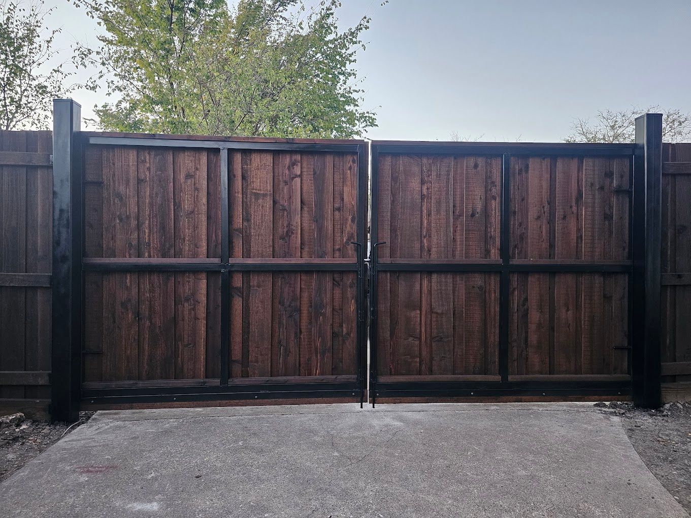 Closed wooden double gate with dark posts and a paved driveway in front