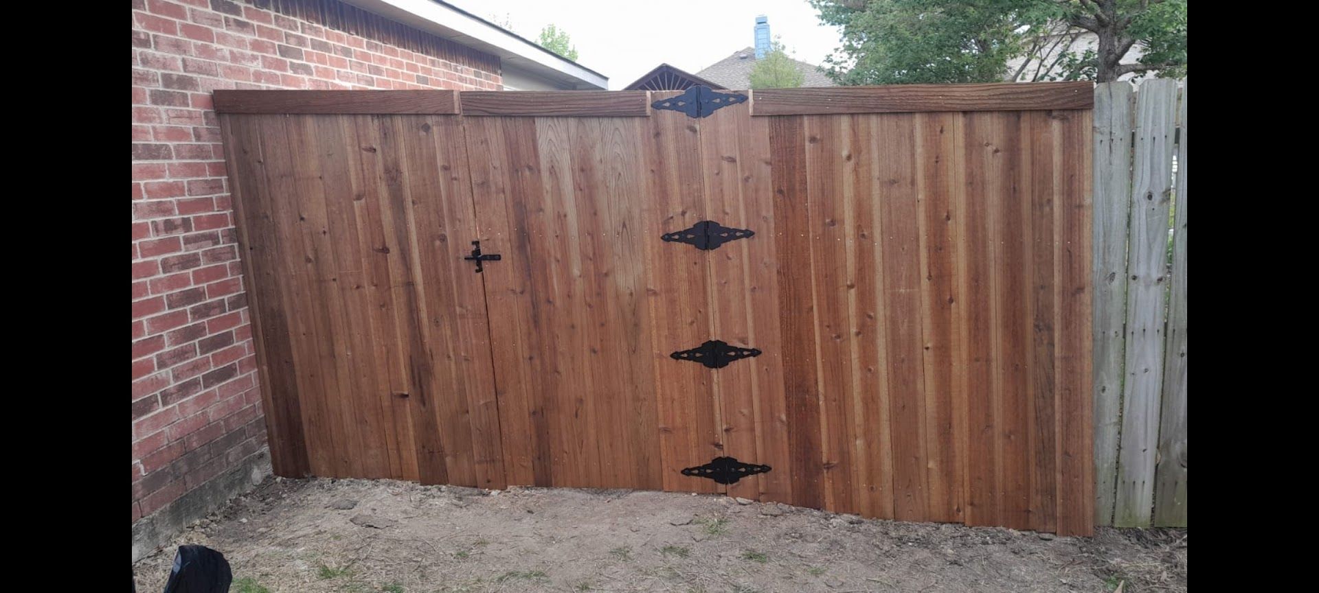Wooden fence gate between brick walls with black hinges and latch