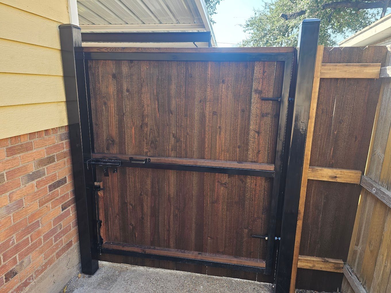Wooden privacy gate with black framing beside a brick house and fence