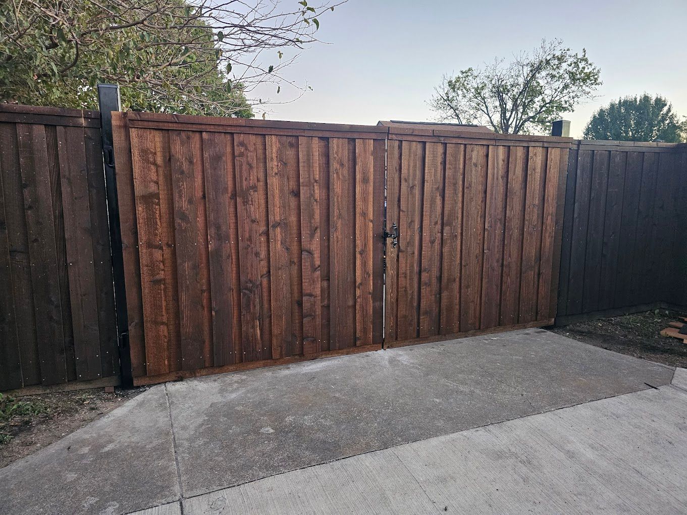 Brown wooden fence with dark side panels along a concrete driveway under a cloudy sky