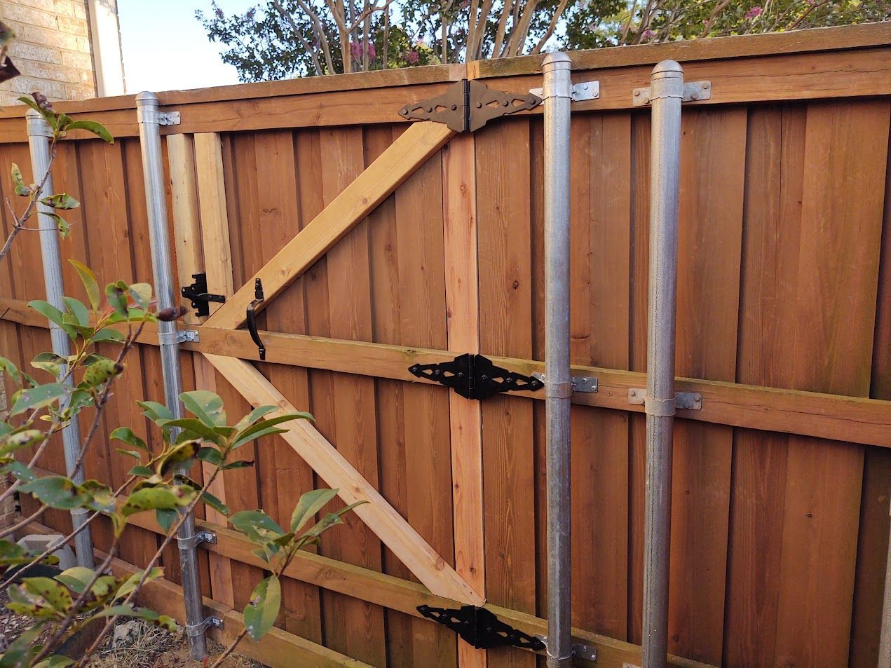 Wooden backyard gate with diagonal bracing and black latches on a tan fence