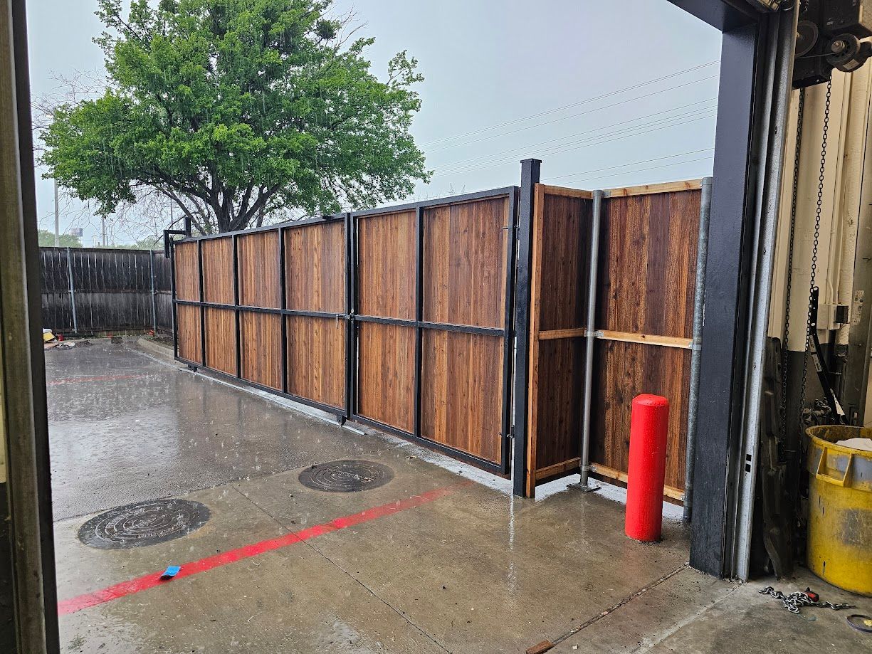 Rainy parking area with wooden fence, tree, and red bollard beside an industrial doorway